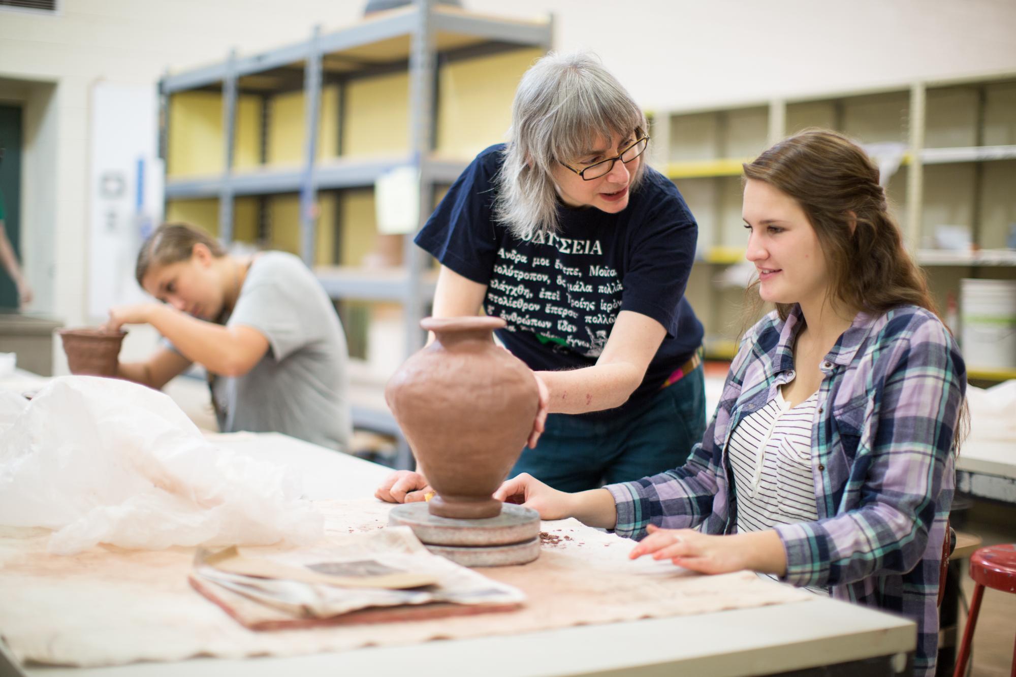 student and faculty interacting while making pottery